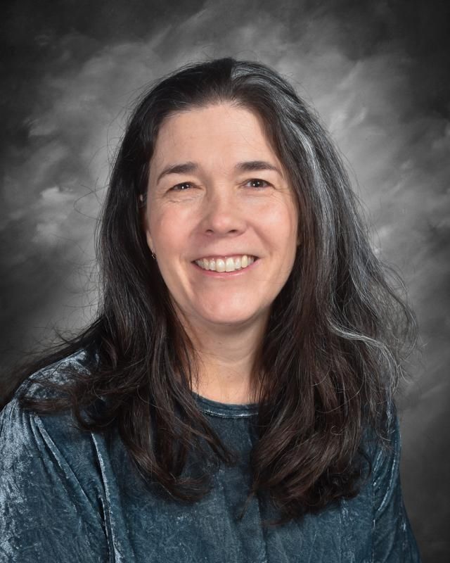 A woman in a black and white striped shirt is smiling in front of a blue background.