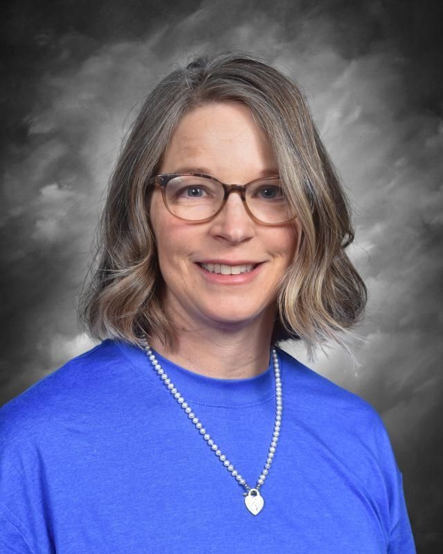 A woman wearing glasses and a pink scarf is smiling for the camera.
