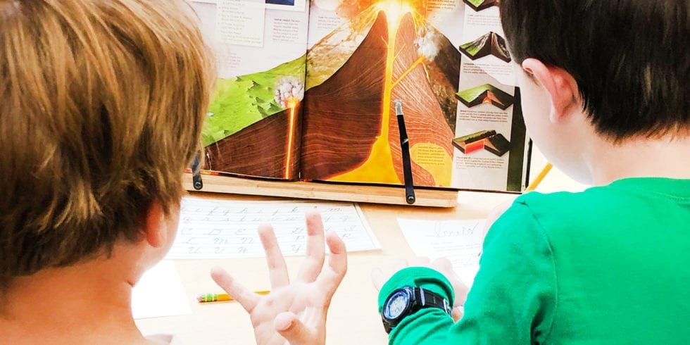Two young boys are sitting at a table looking at a geology book.