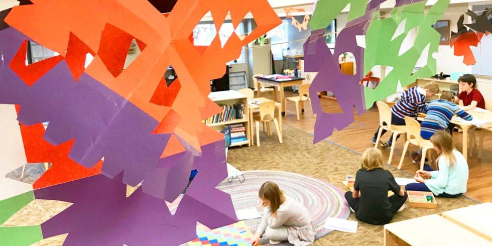 A group of children are sitting on the floor in a montessori classroom.
