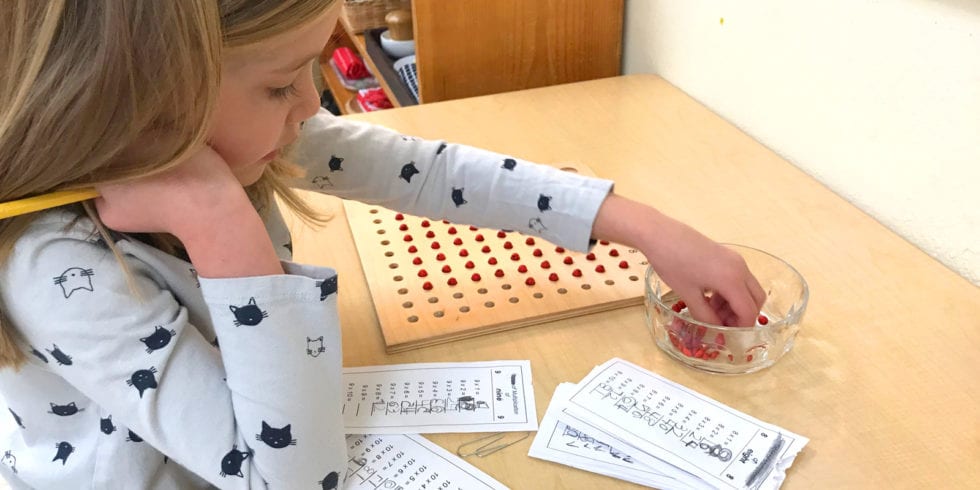 A little girl is sitting at a table working with montessori math materials