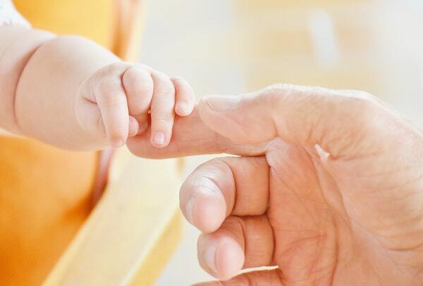 A baby is holding a man 's finger.