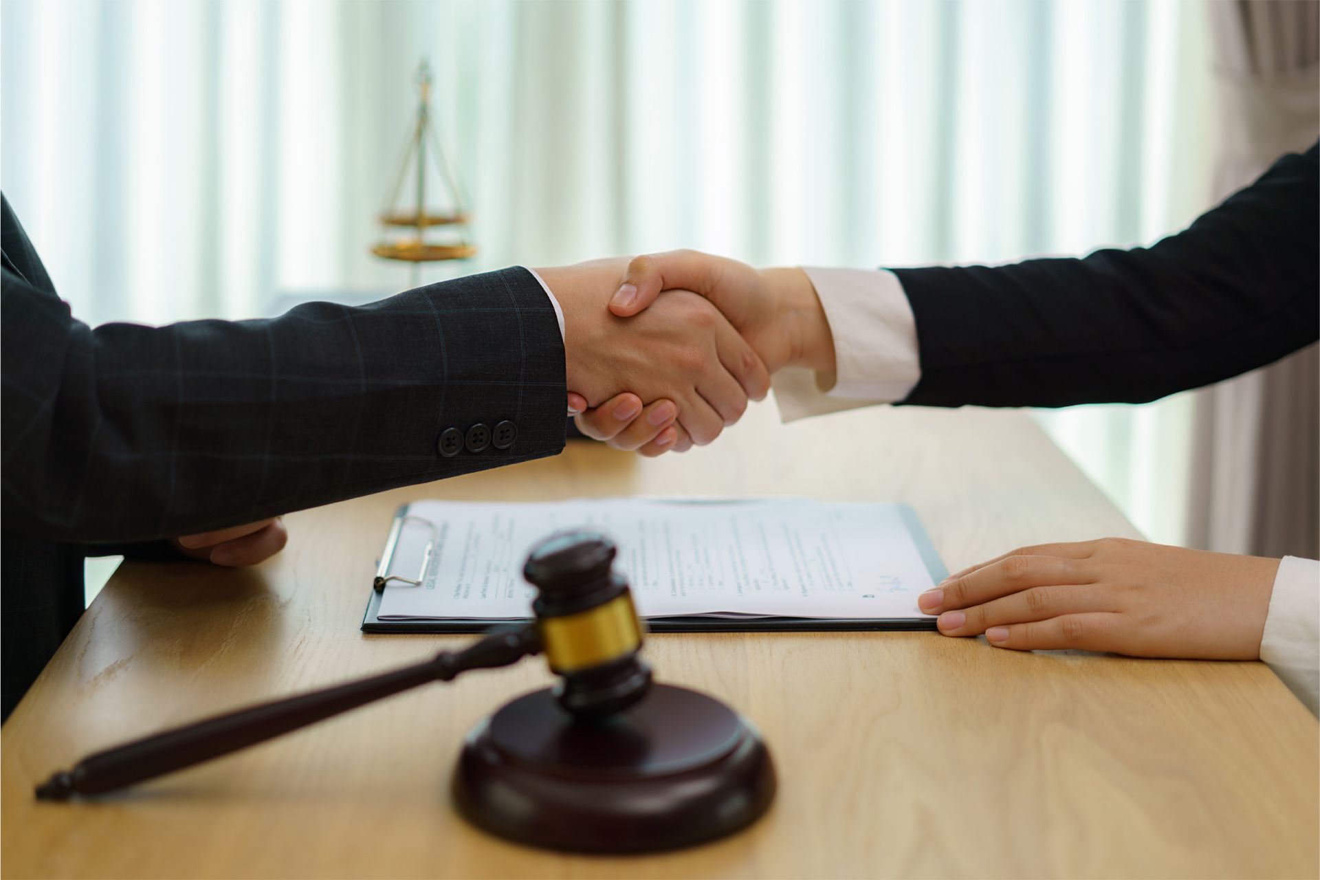 Two people shaking hands over a legal document on a table; a gavel is in the foreground.