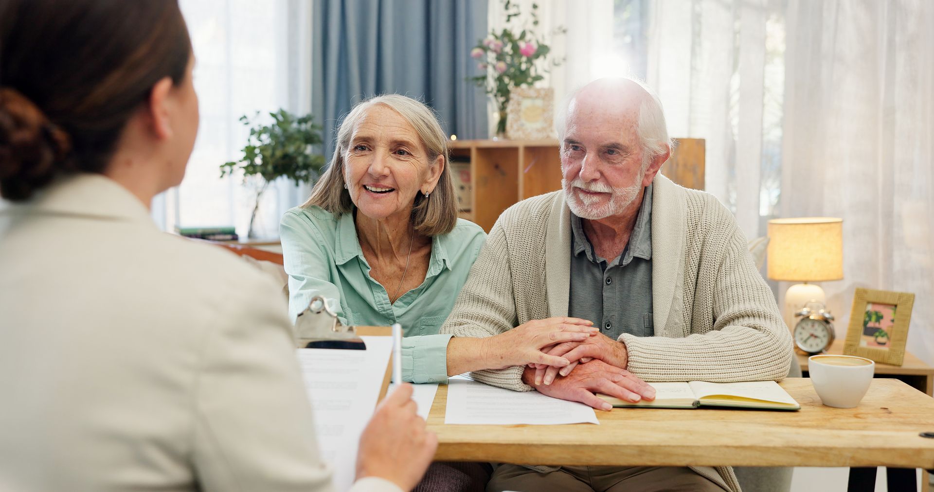 A woman in a lab coat reviews paperwork with an elderly couple, who are holding hands, indoors.