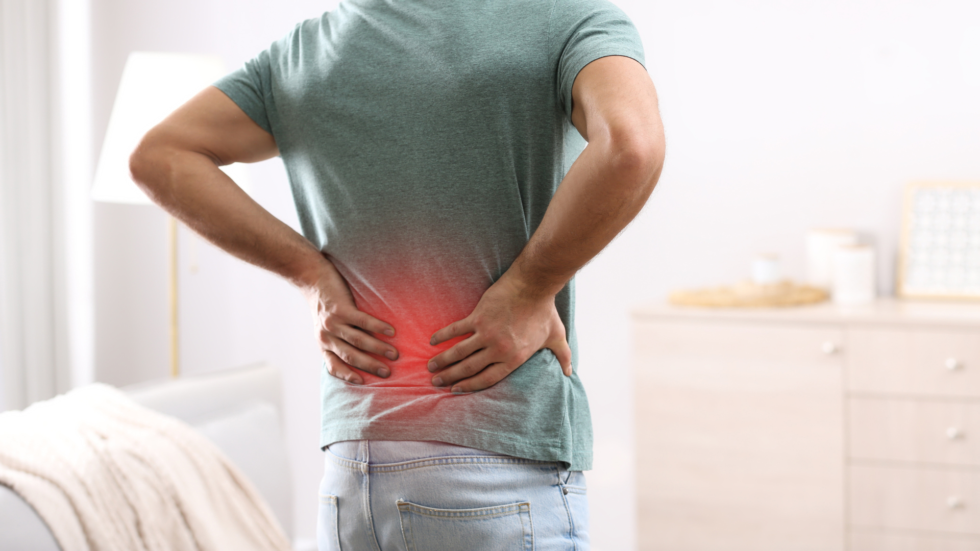 a man is holding his back in pain while standing in a living room .