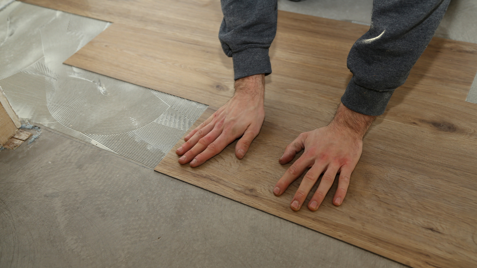 A person installs a wood-look vinyl plank onto a floor with applied adhesive.