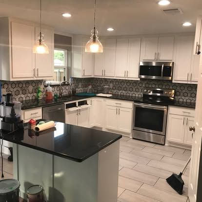 A kitchen with white cabinets , stainless steel appliances , and a black counter top.