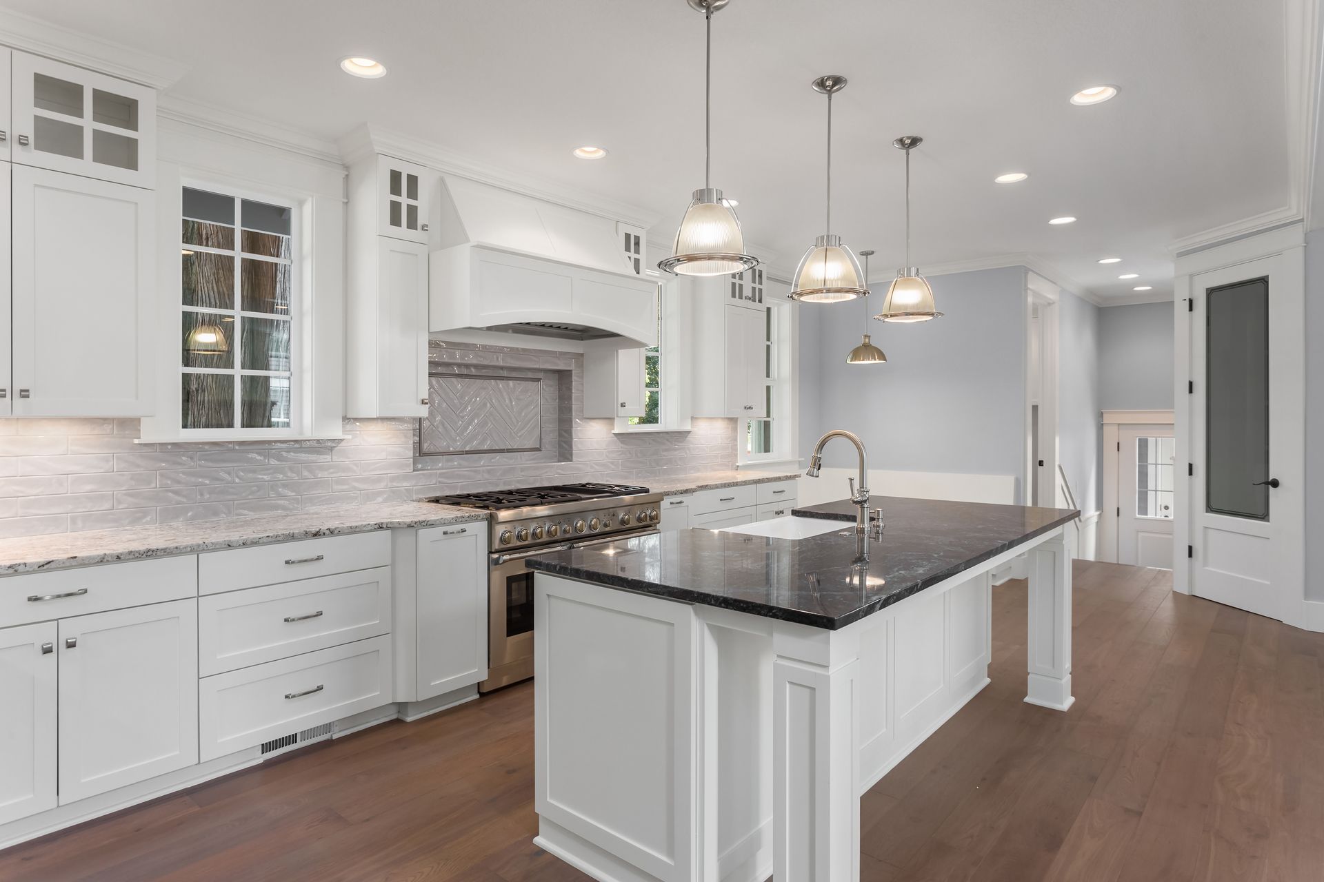 Modern kitchen with white cabinetry, a dark granite island, and three glass pendant lights over hard