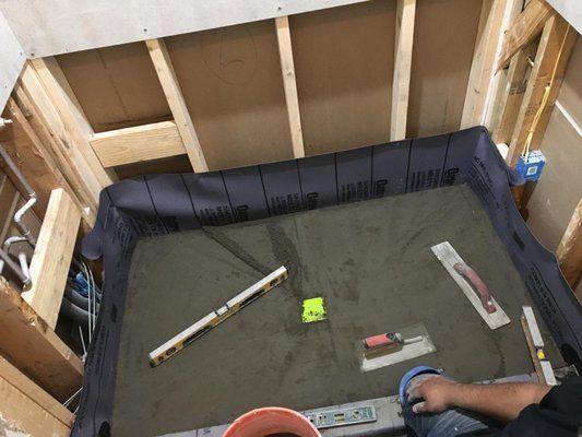 A man is laying concrete on the floor in a room.