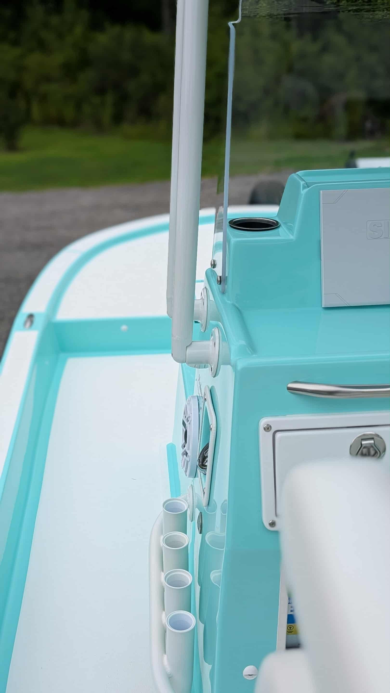 Aqua and white boat cockpit with rod holders, steering, and a windshield.