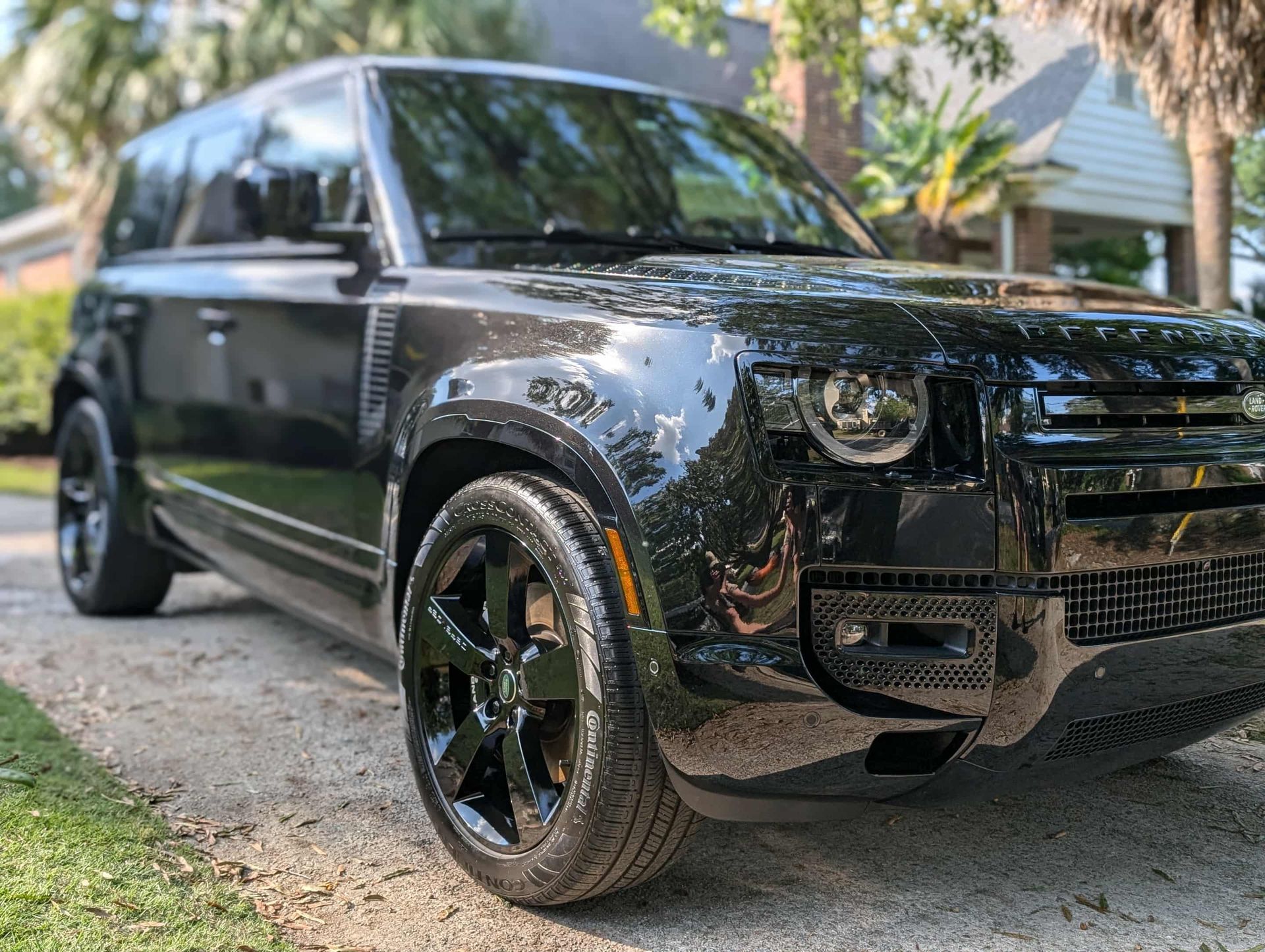 Black Land Rover Defender SUV parked on a driveway, shiny black wheels.