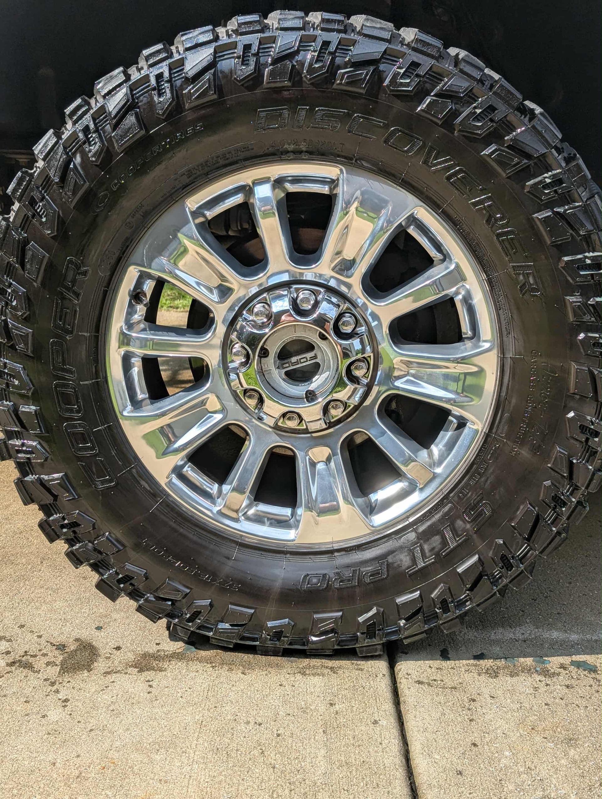 Shiny chrome wheel on a black truck tire, showing tread pattern, parked on a concrete surface.
