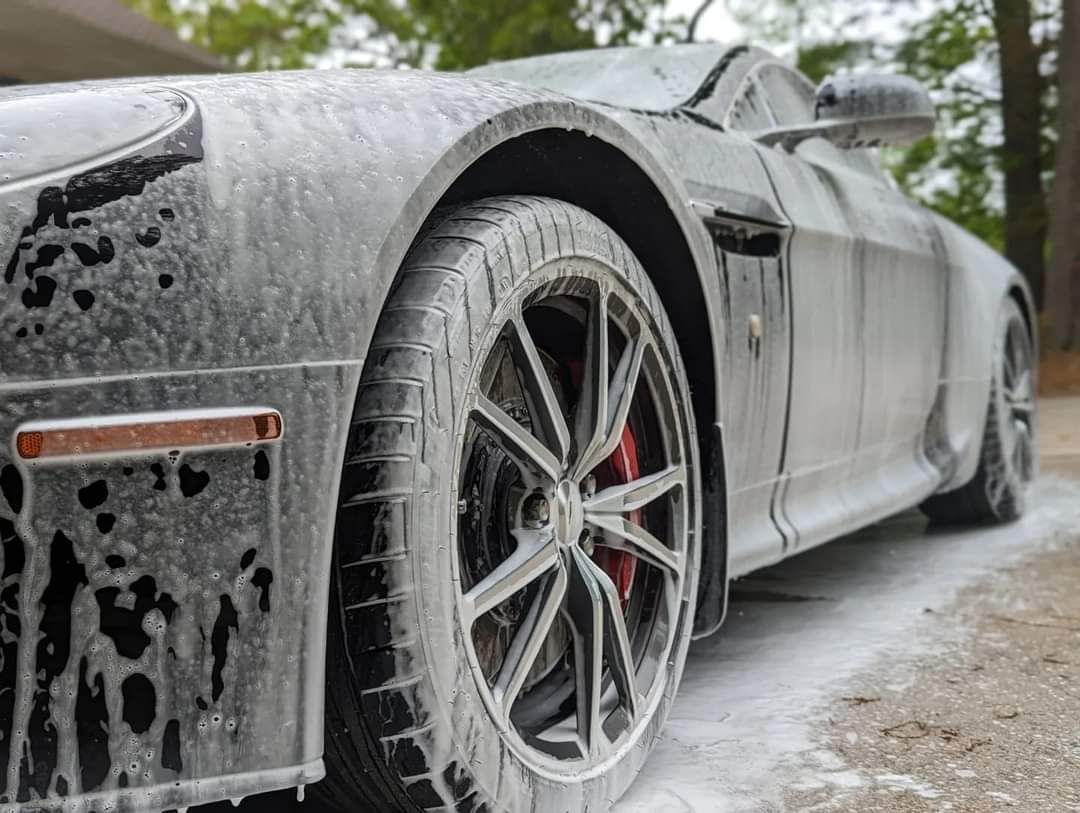 Sports car covered in white foam, undergoing a car wash.