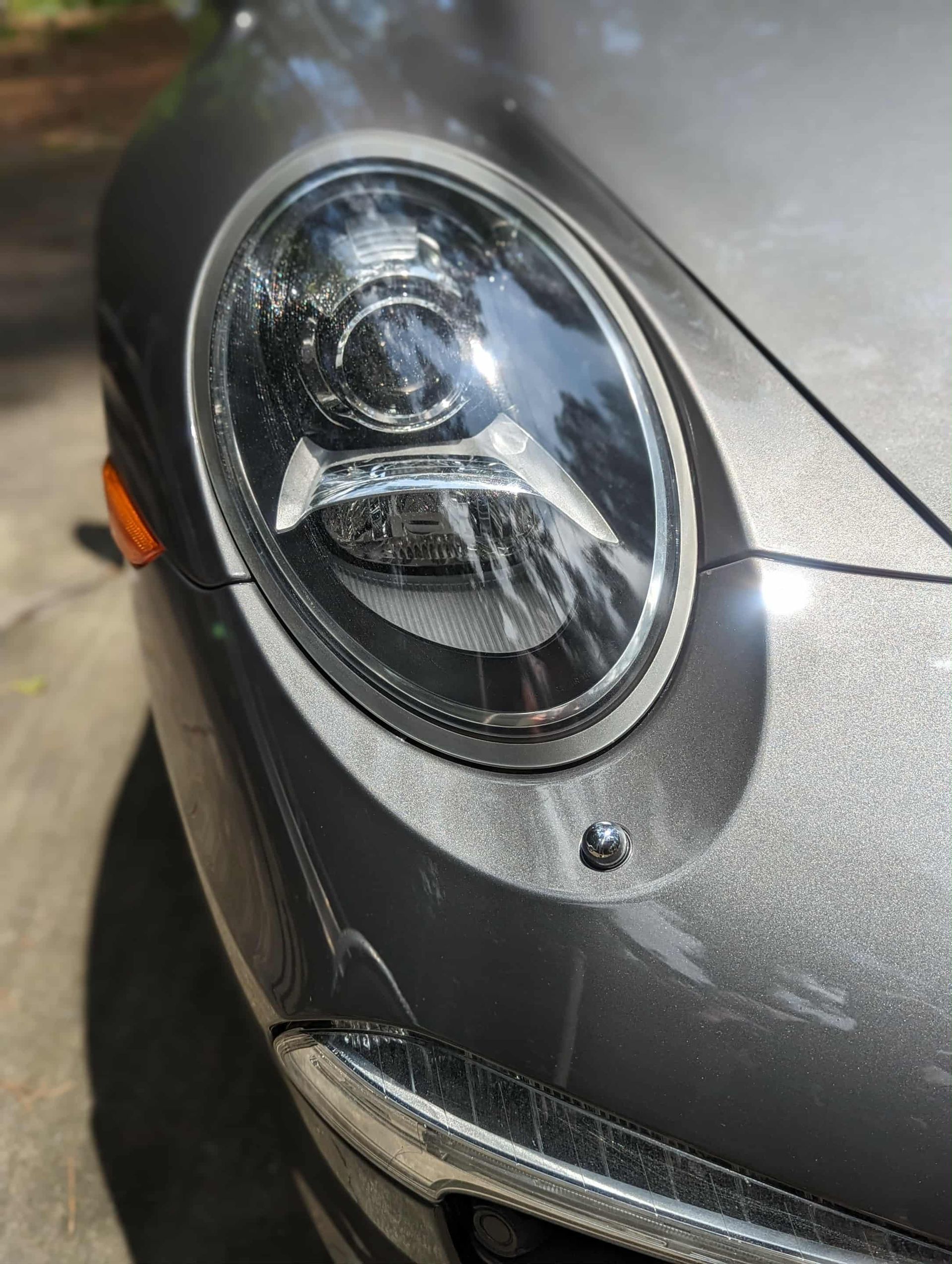 Gray Porsche car headlight, close-up with dirt and road grime.