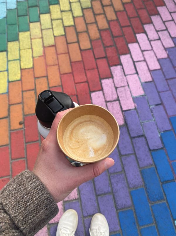 Hand holding a coffee over a chalk-painted rainbow sidewalk
