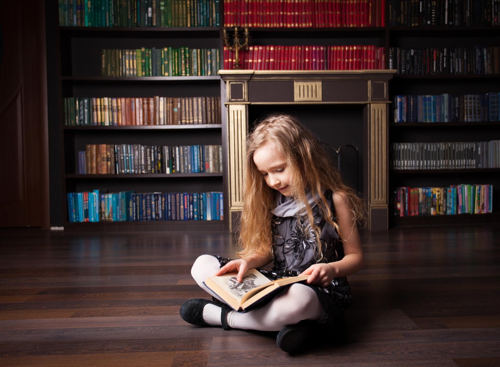 A little girl is sitting on the floor reading a book in a library. A little girl is sitting on the floor reading a book in a library.