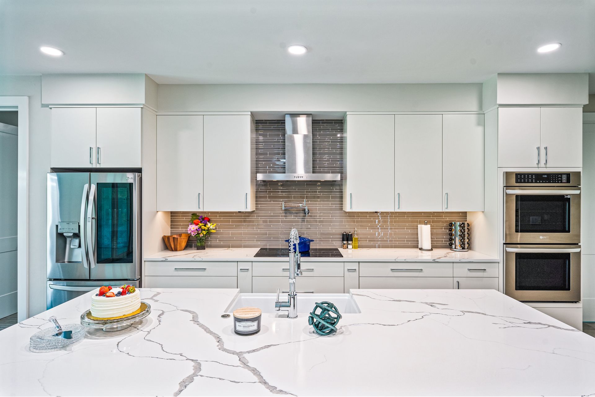 A kitchen with white cabinets, stainless steel appliances, a large island with a cake on it.