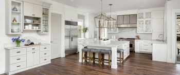 A kitchen with white cabinets, hardwood floors, stools and a large island. A kitchen with white cabinets, hardwood floors, stools and a large island.