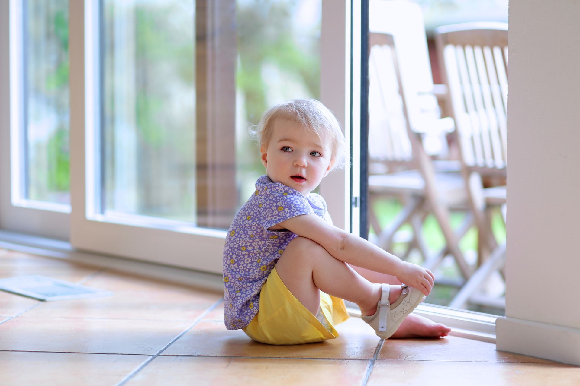 A little girl is sitting on the floor in front of a window. A little girl is sitting on the floor in front of a window.
