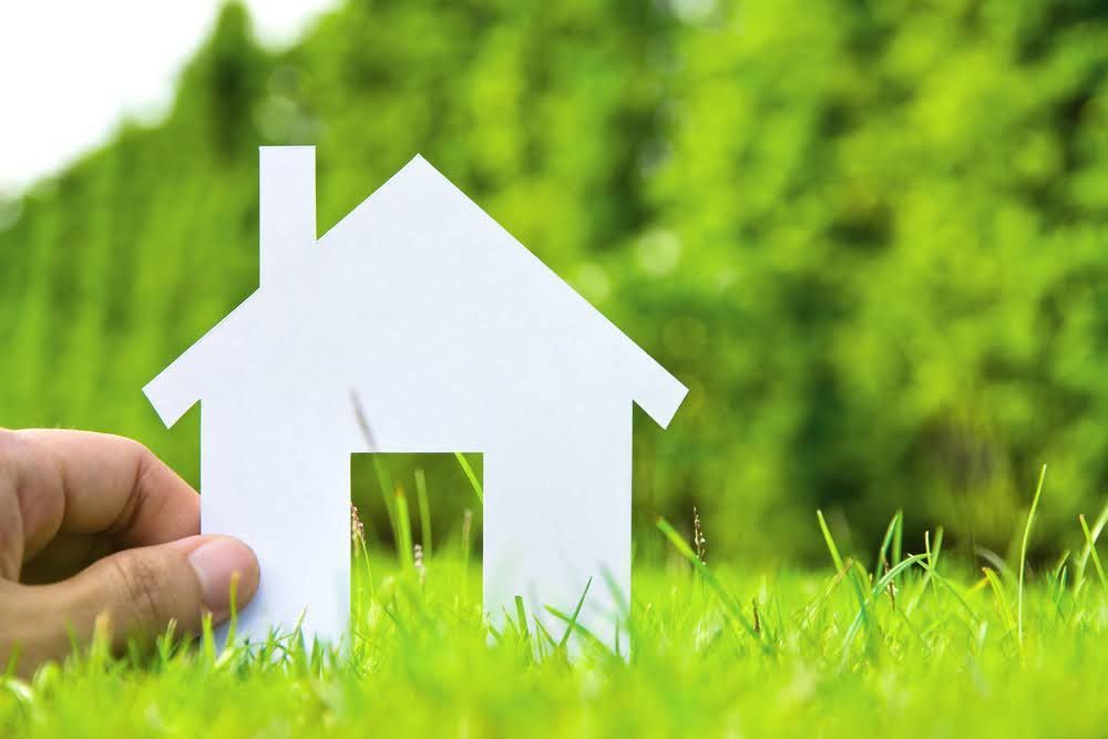 A person is holding a paper house in the grass. A person is holding a paper house in the grass.