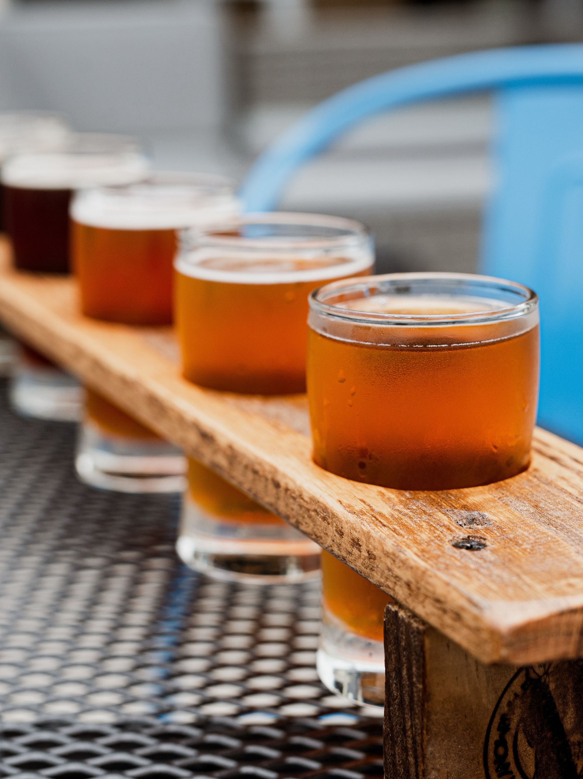 A row of shot glasses filled with beer on a wooden tray.