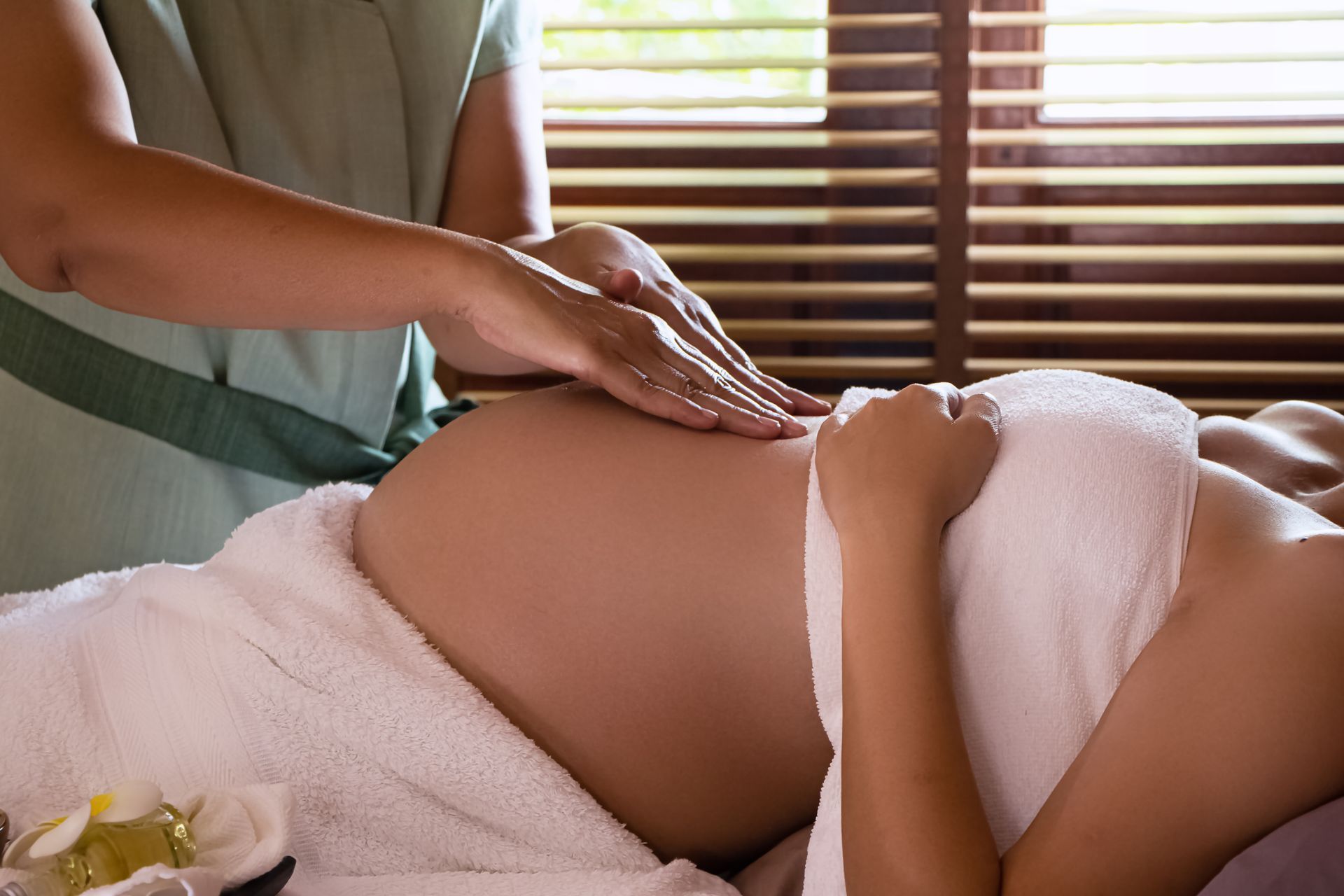 Person receiving a back massage in a spa room with warm light and wooden blinds