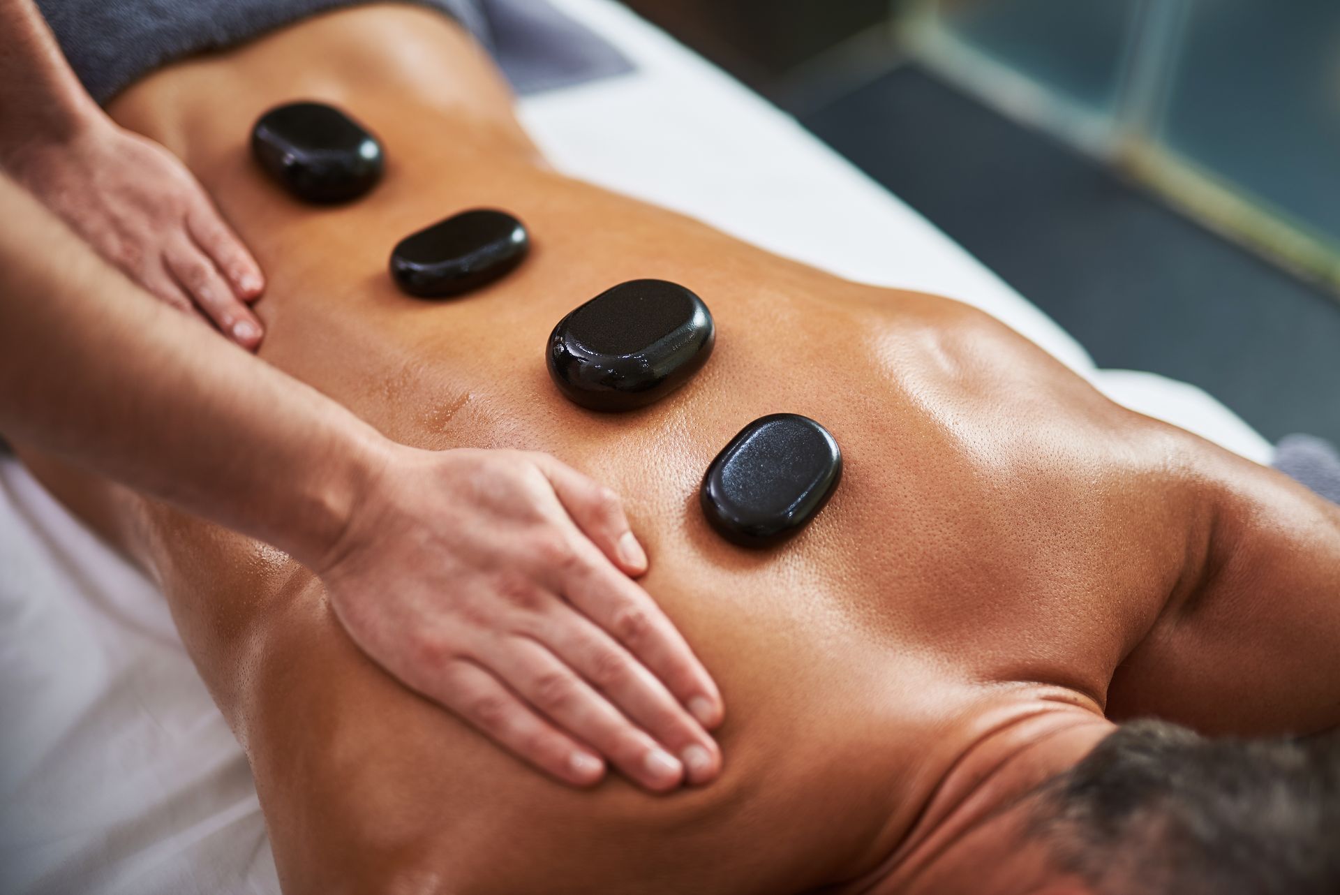 Hot stone massage on a person’s bare back with hands applying pressure