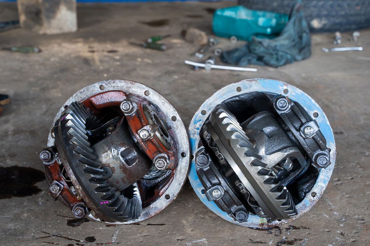 Two open automotive differentials side-by-side on a concrete surface, showing internal gears and housings.