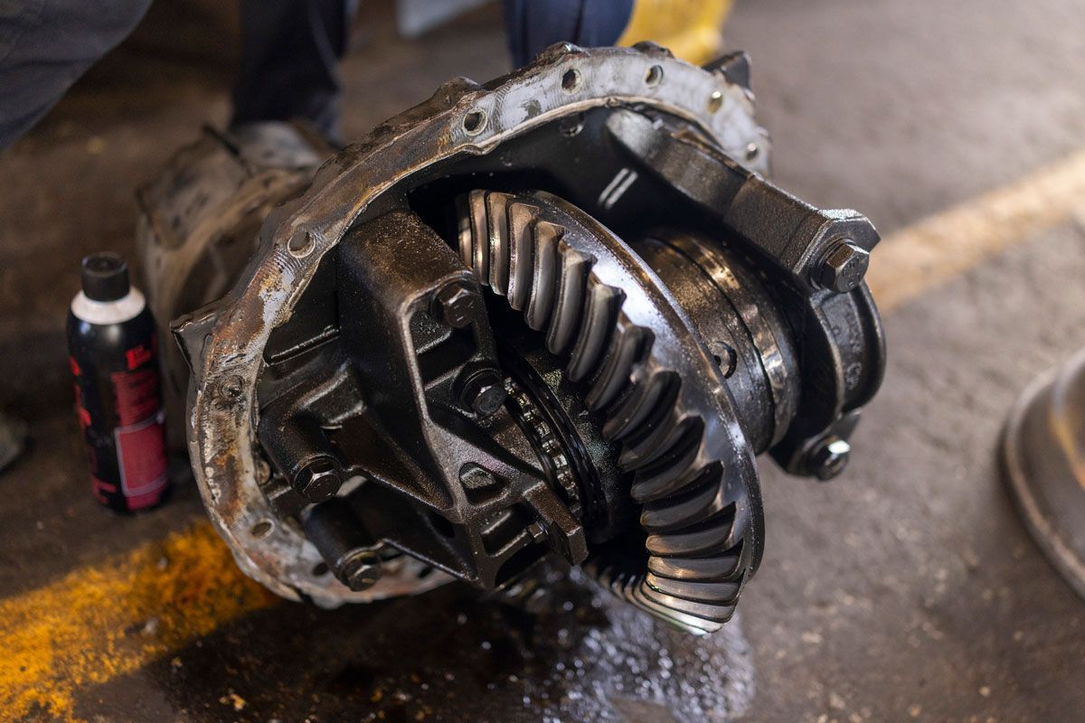 Open differential gear assembly, disassembled. Black metal parts, oil, on a garage floor.
