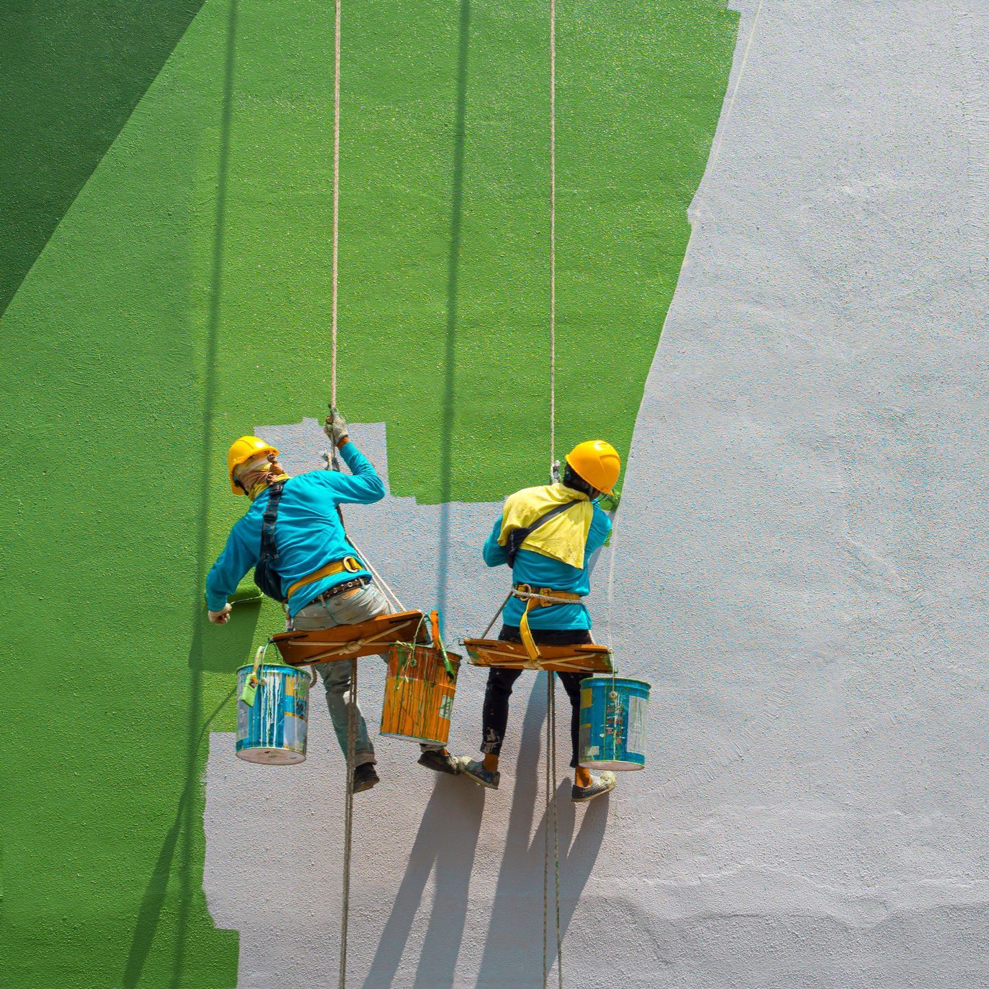 Two people are painting a wall on a rope.