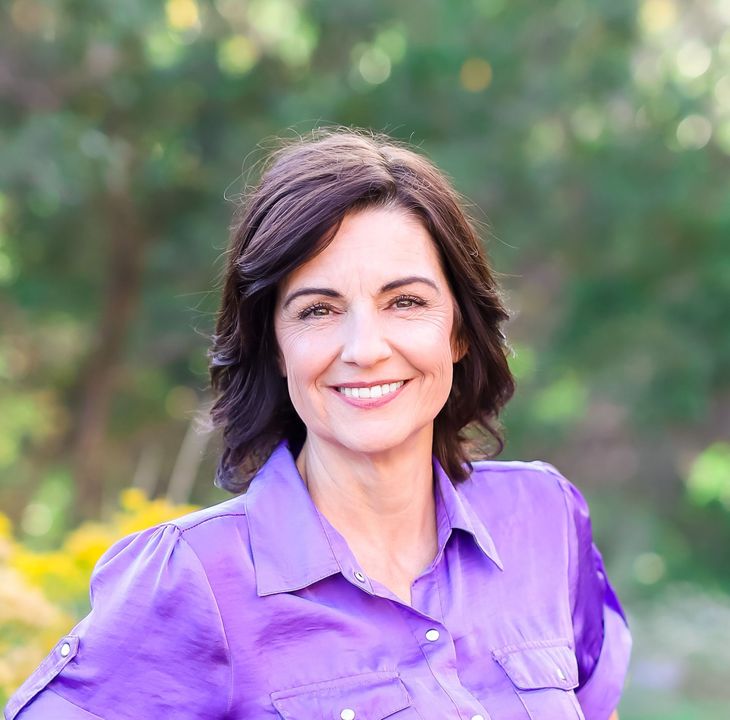 Woman in purple shirt smiles outdoors.