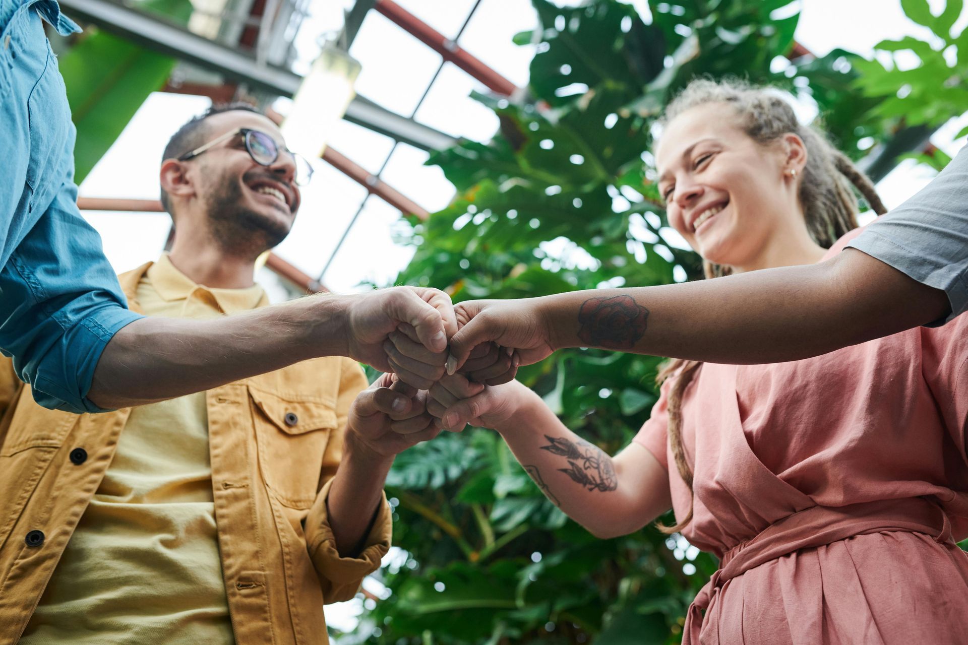 Group of people, smiling, fist-bumping. Green background of plants, outdoors.