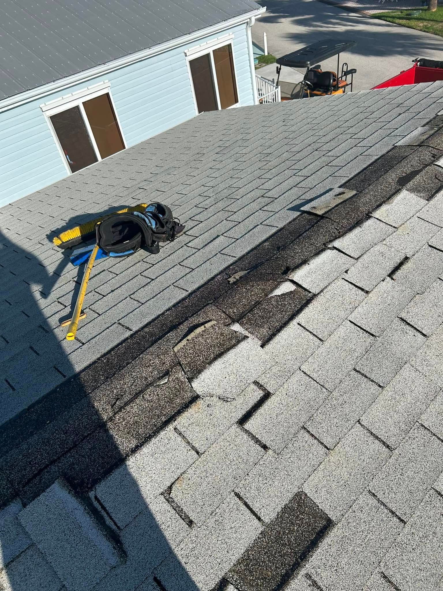 A partially replaced asphalt shingle roof on a sunny day, with a crowbar and tools lying on the roof surface.