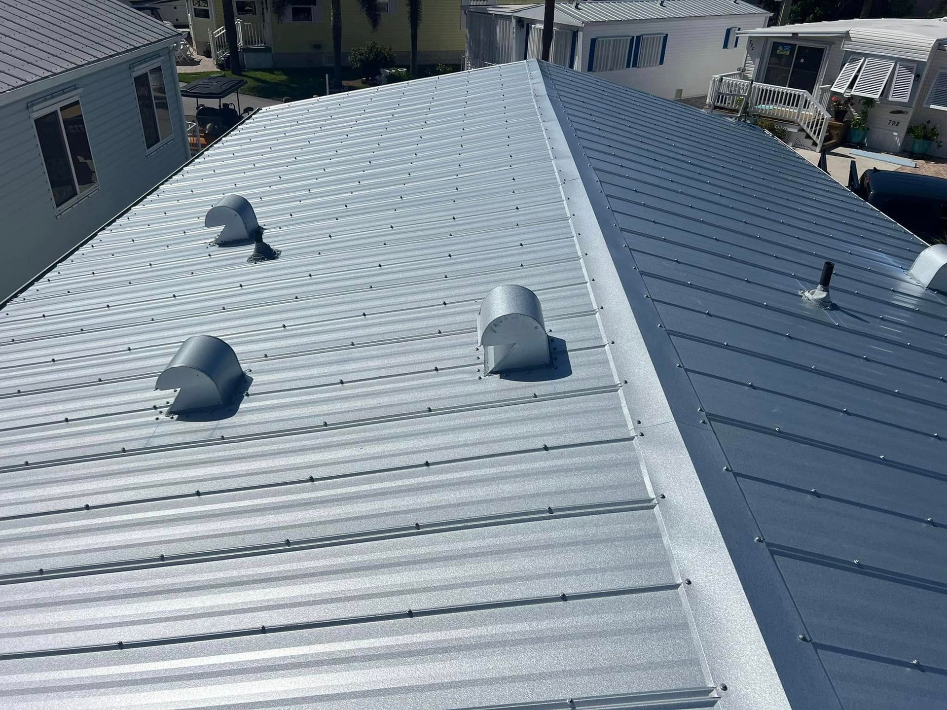 High-angle view of two different styles of metal roofing on a residential building with several ventilation caps.