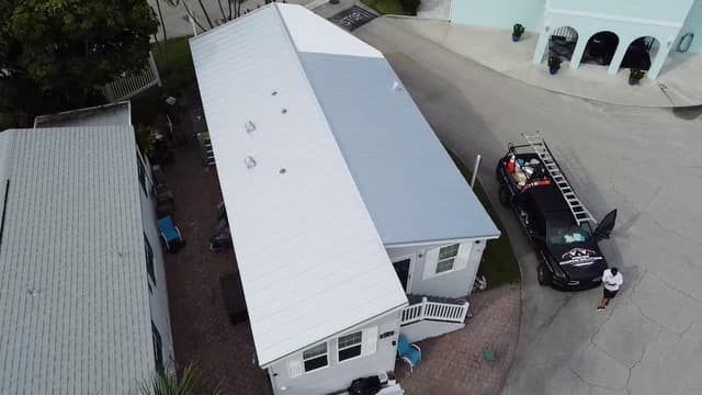 Aerial view of a mobile home with a partially painted white roof, next to a service truck and a person in a parking lot.