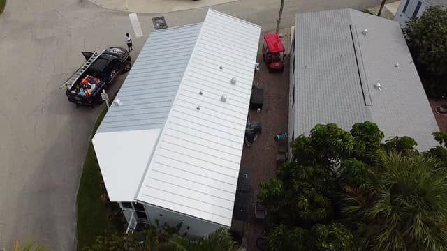 An aerial view showing two adjacent houses with light-colored metal roofs, a dark pickup truck, and a red golf cart.
