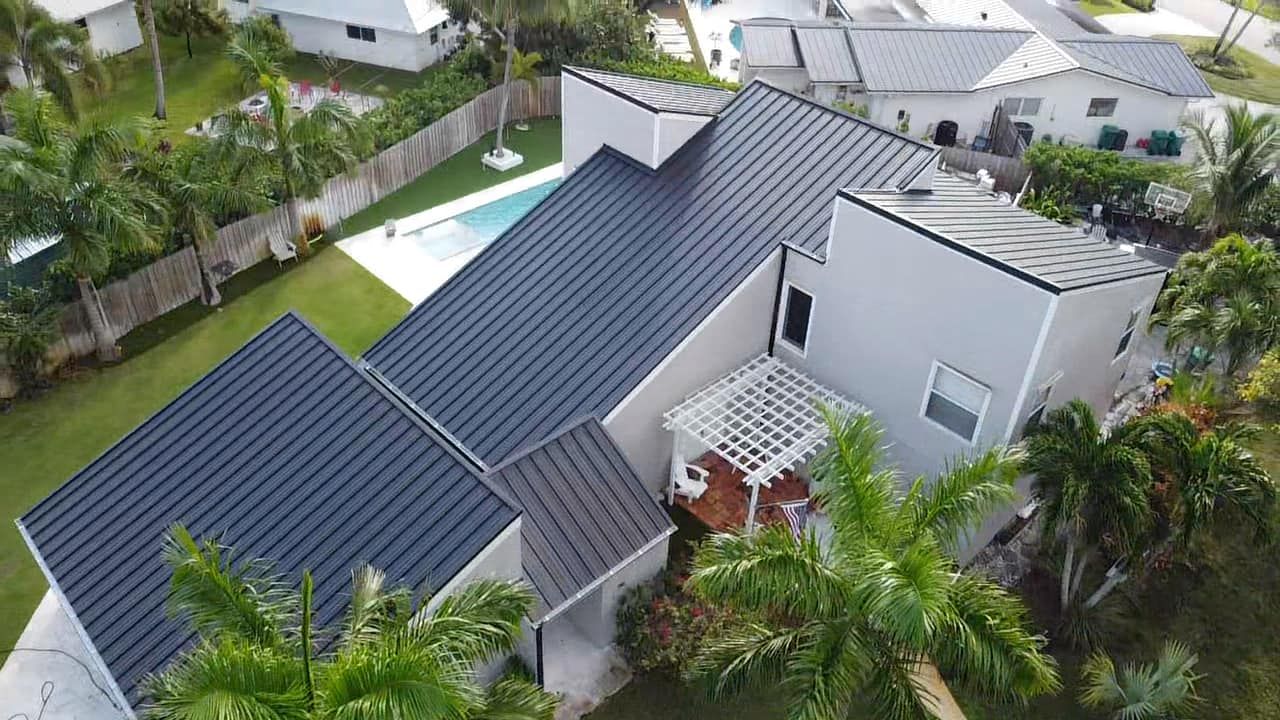 Aerial view of a house with a dark metal roof, backyard pool, pergola, and surrounding trees.