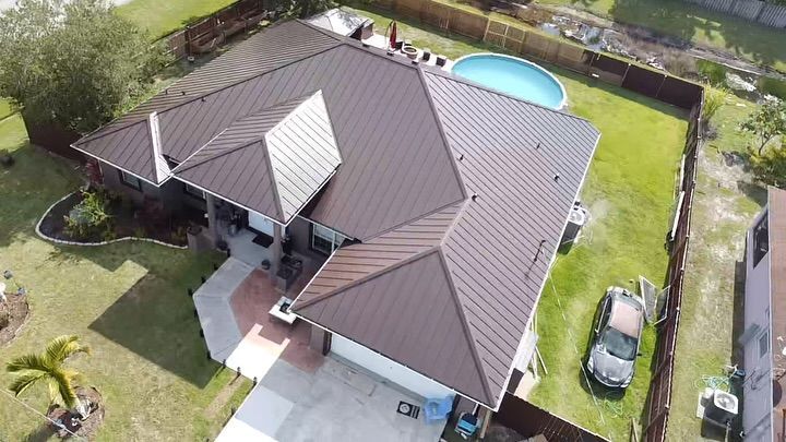 Aerial view of a single-story home with a brown metal roof, a backyard pool, and a car parked in the driveway.
