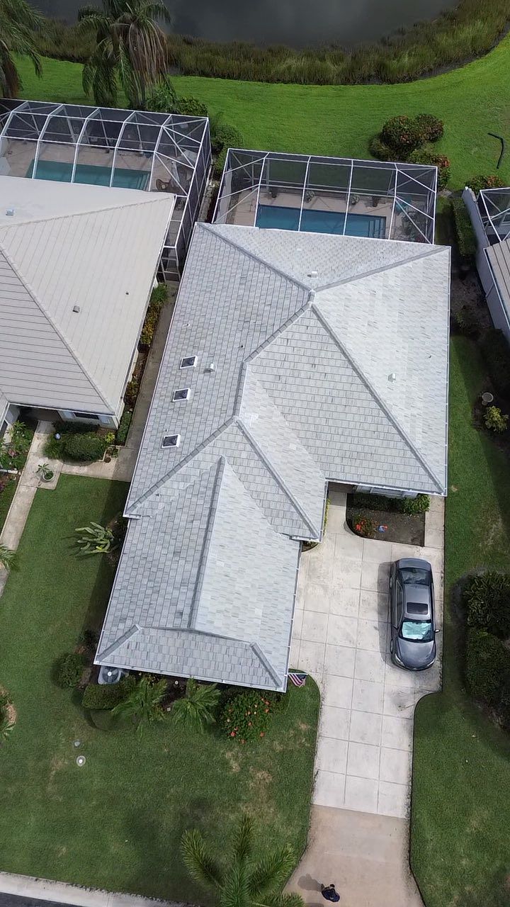 Aerial view of a residential house with a gray shingled roof, pool cage, driveway, and a parked car.