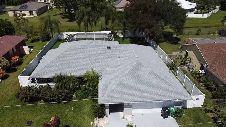 Aerial view of a residential house with a gray roof and a screened-in pool enclosure in a suburban backyard.
