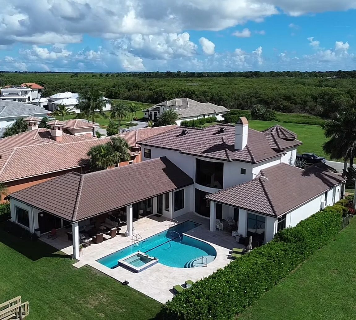 Aerial view of a white, two-story house with a brown tiled roof, a swimming pool, and a lush backyard.
