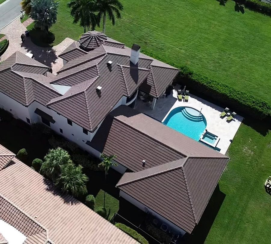 Aerial view of a large residential home with a brown tile roof, pool, and expansive green lawn.