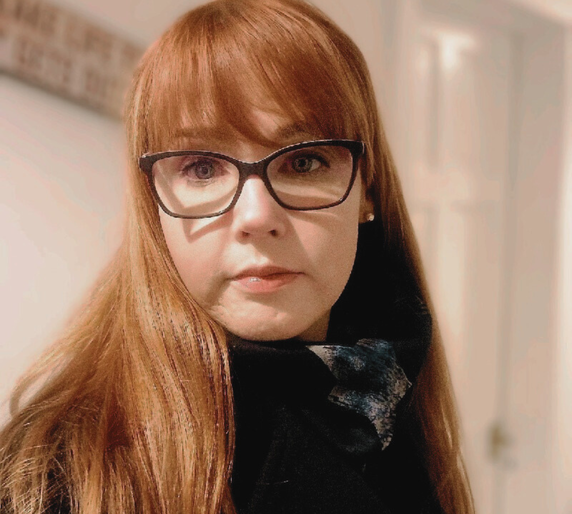 Eve Rusc wearing glasses and a scarf looks at the camera