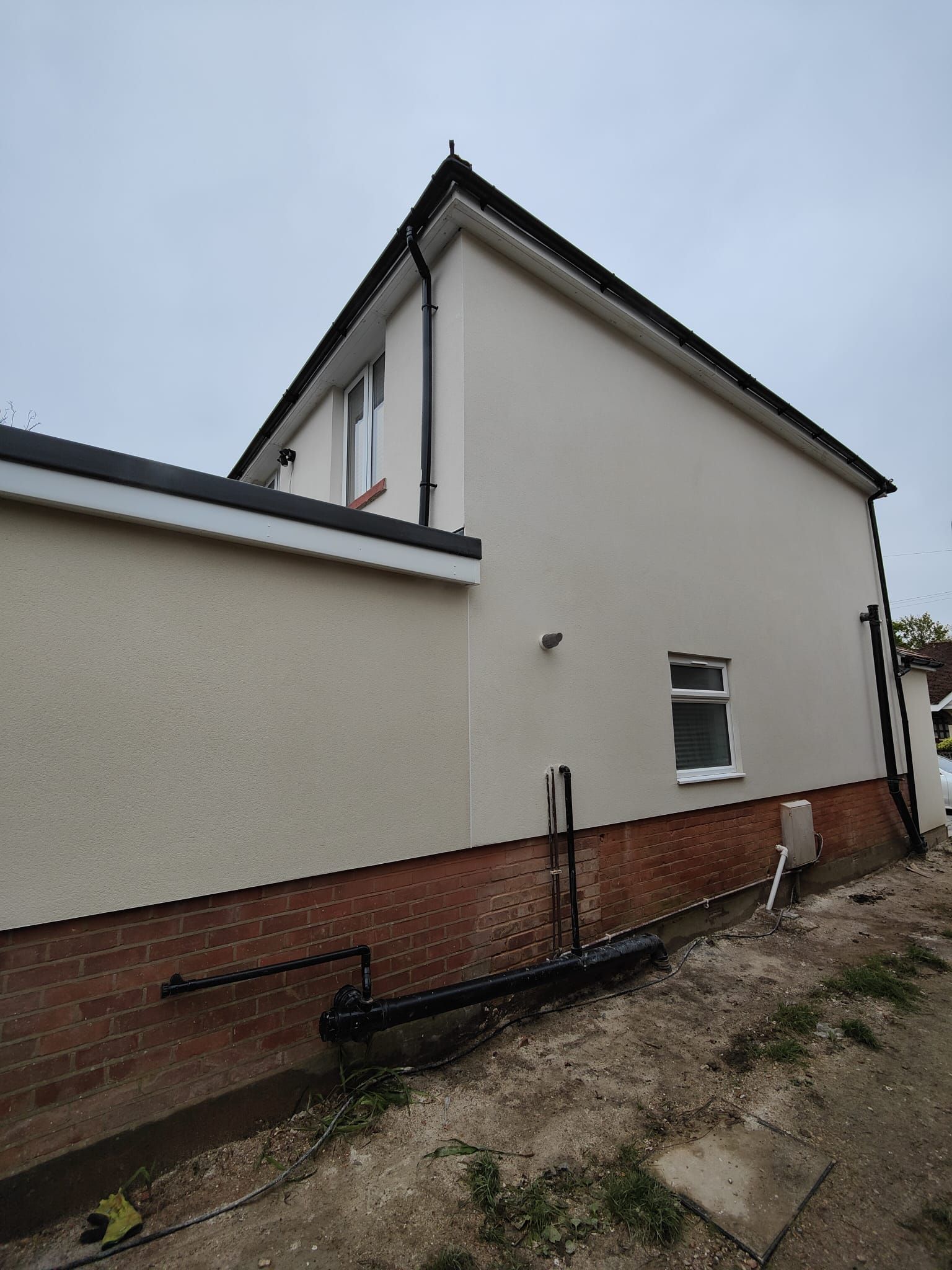 A white house with a brick wall and a black gutter