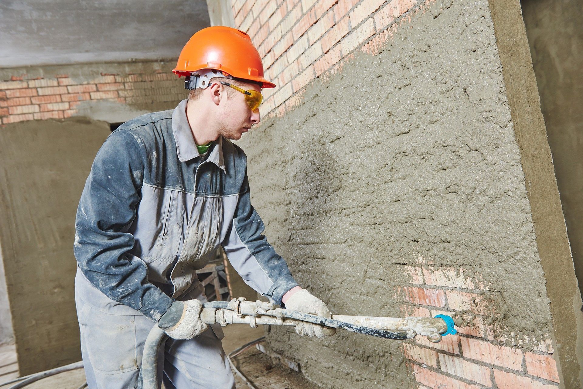 A man wearing a hard hat and safety glasses is plastering a brick wall.