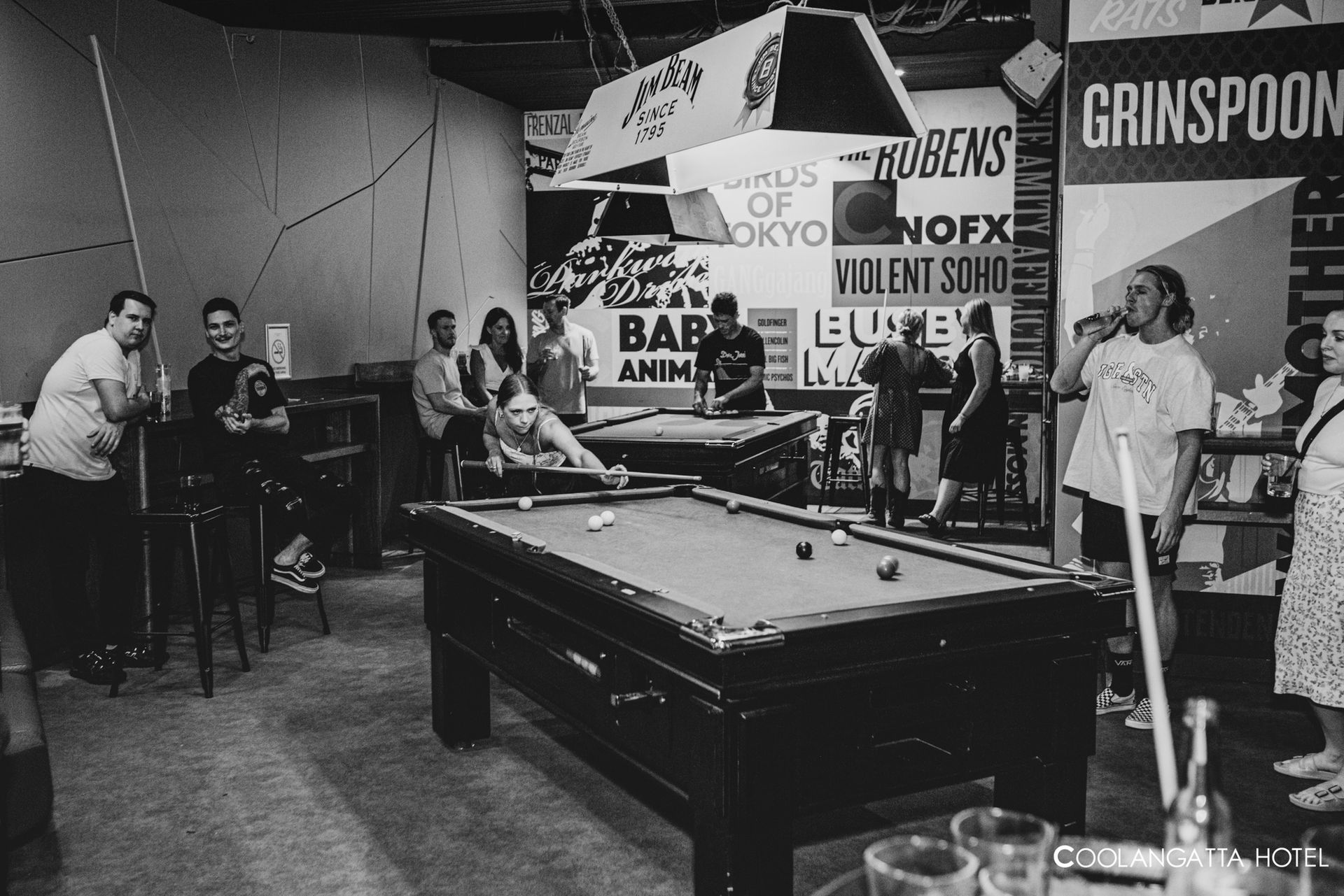 People playing pool in a crowded black-and-white hall with banners and spectators