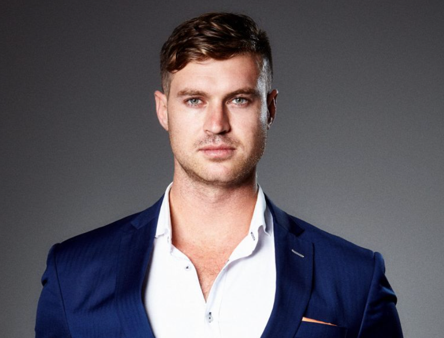 Studio portrait of a man in a navy blazer and white shirt against a gray background