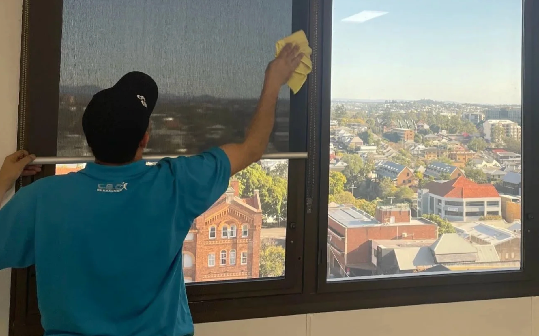 Person cleaning a large window with a cloth, overlooking a bright city view