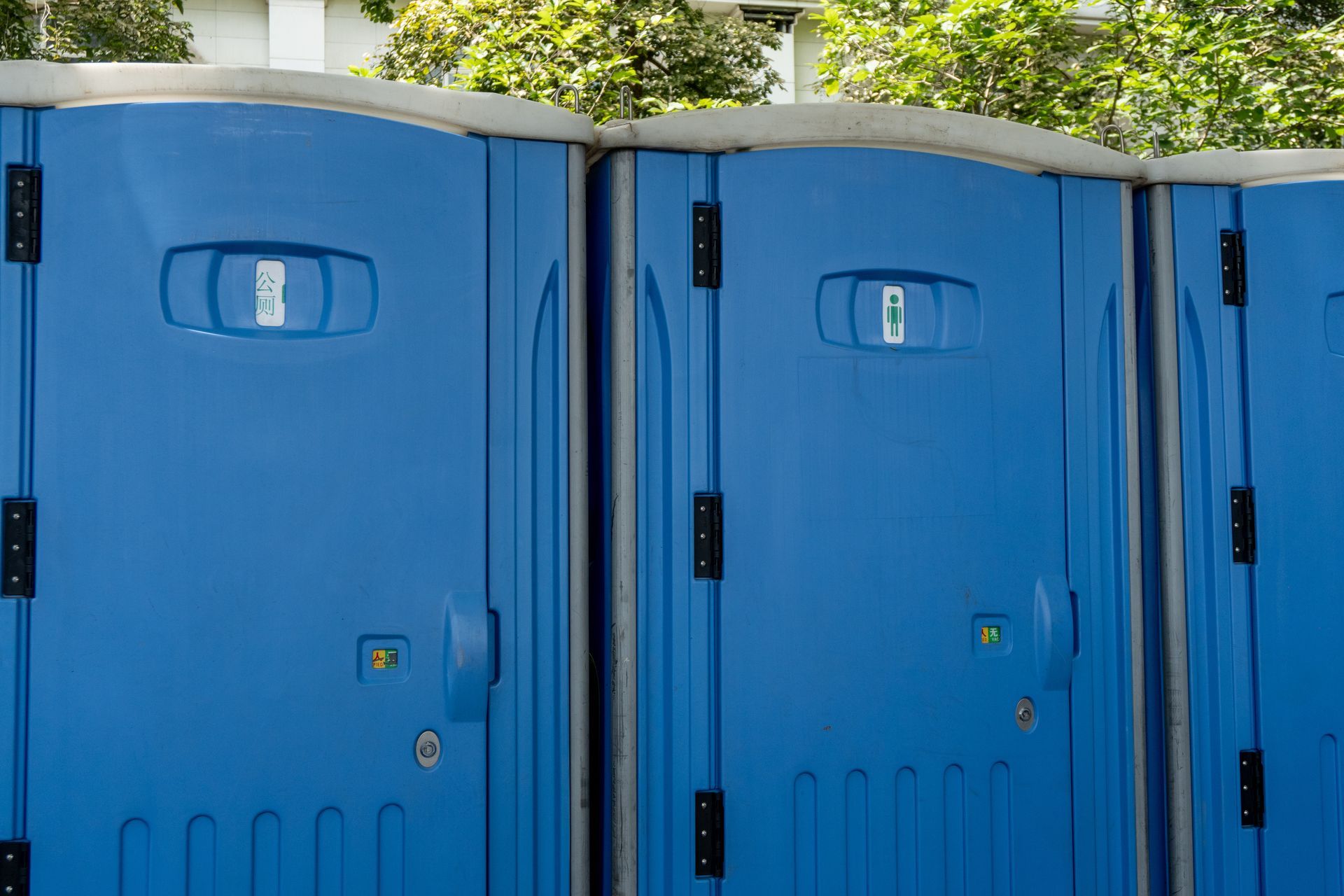Blue portable restroom units standing side by side outdoors near greenery.
