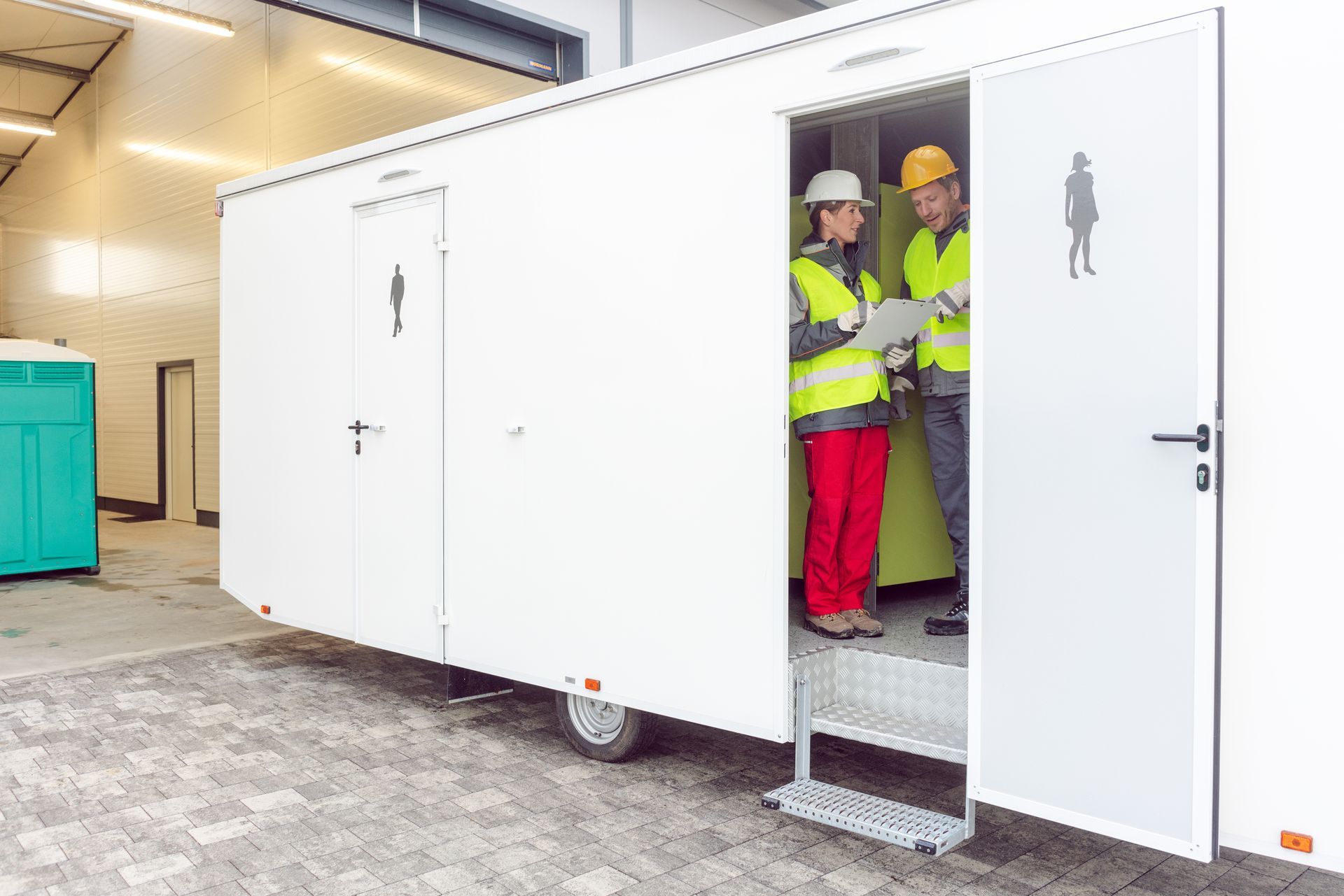 Workers inspecting mobile portable restroom trailer unit with checklist on construction site.